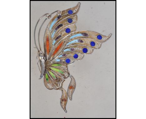 A silver filigree vintage butterfly brooch from the mid 20th century. The wings are decorated in various coloured enamels wit