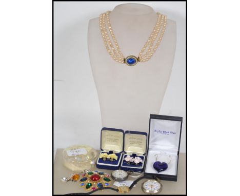 A collection of costume jewellery to include; A faux pearl triple corded necklace with blue cut glass clasp; A silver pocket 