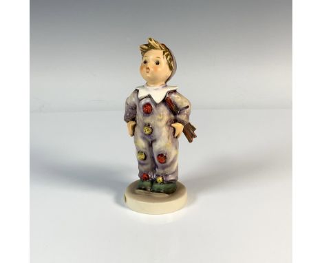 A figure of a boy wearing a colorful clown outfit decorated with moons and pom-poms. M.I. Hummel impressed. Goebel backstamp.