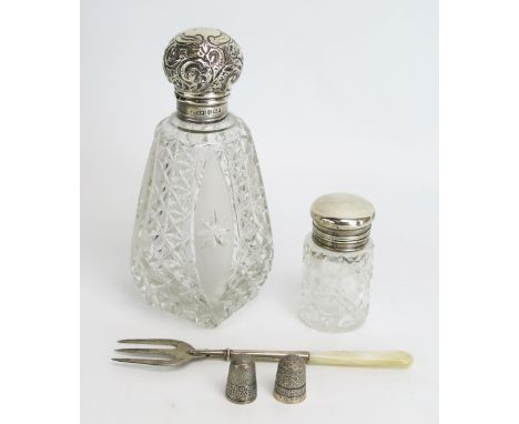 A clear glass and silver mounted scent bottle, a smaller silver topped jar, two thimbles and an olive fork. 