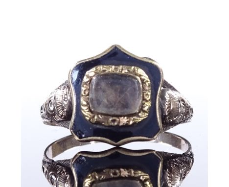 A 19th century unmarked gold and black enamel mourning ring, central glass-fronted shield-shaped panel in relief floral surro