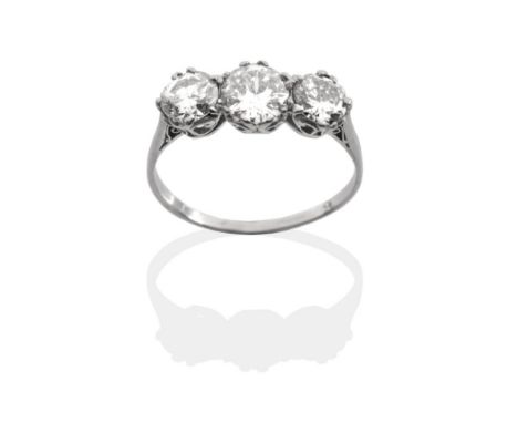 A Diamond Three Stone Ring, three graduated round brilliant cut diamonds in white claw settings above a carved scroll gallery