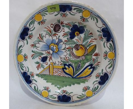 A Delftware charger painted with flowers and a bridge in shades of green, blue, iron red, ochre and manganese. 14' diam