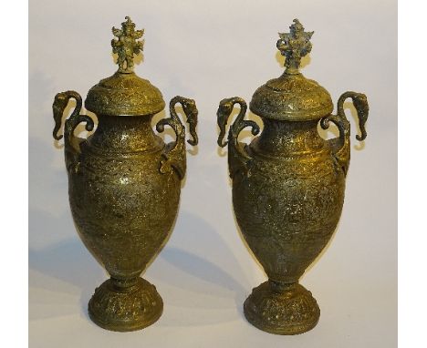A pair of large Indian brass vases, with deity finials to the covers and elephant trunk handles, decorated with raised panels