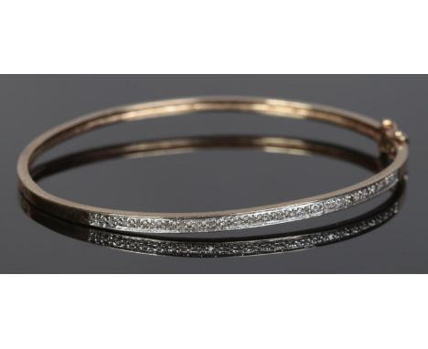 A 9ct Gold hinged bangle set with a band of small diamonds. Stamped 375 to inside of bangle. Total weight: 7.87g  One stone m