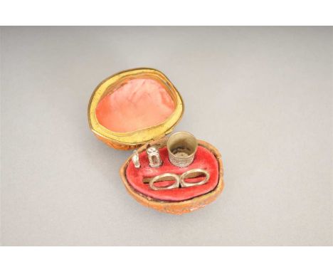 A mid 19th century miniature sewing etui, for a child or a doll, cased in a walnut shell, opening to reveal a felt an silk li