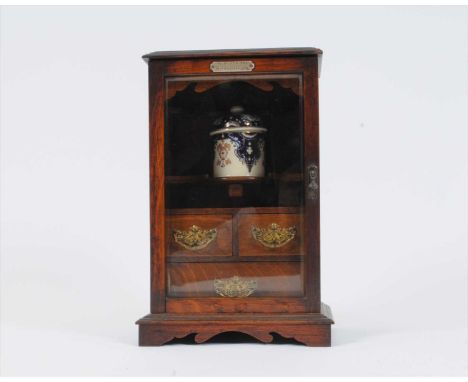 A late Victorian oak smoker's cabinet, the bevelled top over-hanging a bevelled glazed panelled door, inset with a silver-pla