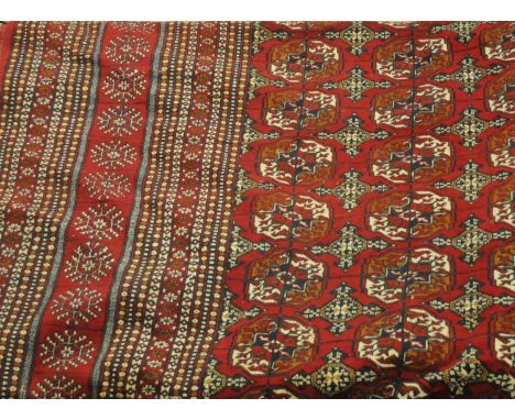 An Afghan Bukhara carpet, the raspberry field, with columns of quartered guls, enclosed by multiple borders, 443cm x 310cm