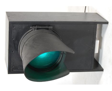 A contemporary recased green light traffic light lamp. The light having a green plastic cover shade with overhanging black sh