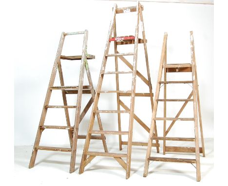 A set of three vintage 20th century wooden A-frame industrial step ladder of a typical form with angular steps. Measures 185 