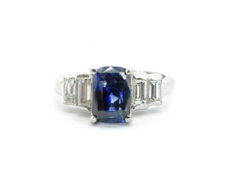 An Art Deco platinum sapphire and diamond ring. The ring set with a cushion cut sapphire (approx 8.9mm x 6mm x 7mm deep) flan