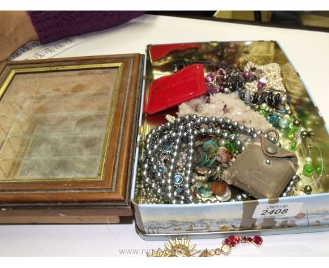 A small mirror backed four shelf display case and a biscuit tin containing various costume jewellery
