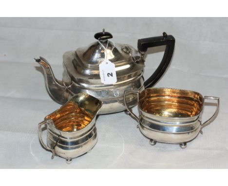 A George V silver three piece tea service of oblong form on ball feet, comprising teapot, (engraved) sucrier and milk jug. Lo