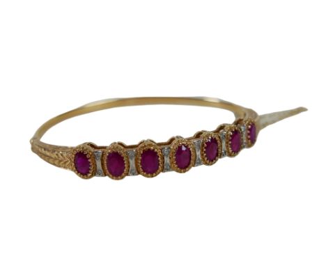 A 9ct gold and ruby hinged bangle, set with seven oval cut rubies, in claw setting, interspersed by twelve brilliant-cut diam