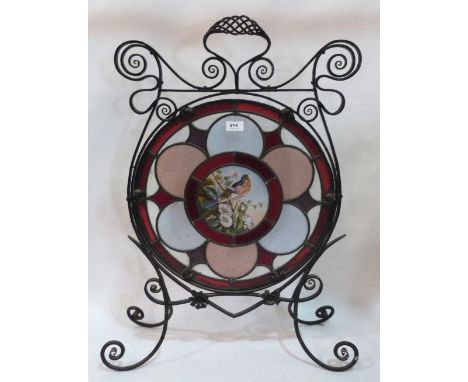 A Victorian wrought iron and stained glass firescreen, the centre pane painted with a bird in prunus. 32' high