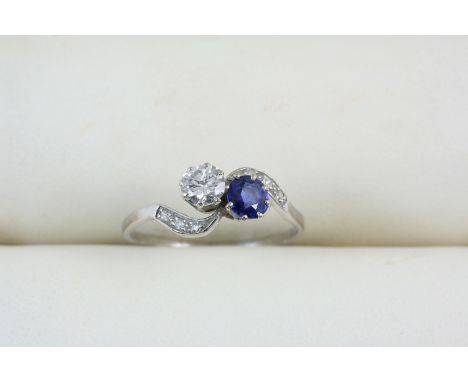 A SAPPHIRE AND DIAMOND CROSS-OVER RING set with a circular-cut sapphire and diamond, with small diamonds set to each shoulder