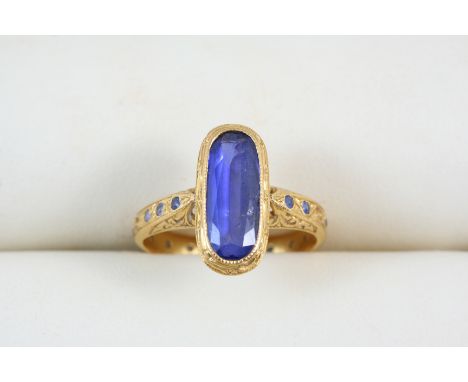 A SAPPHIRE AND GOLD RING the oval-shaped sapphire is set within an engraved gold mount and shank set with circular-cut sapphi