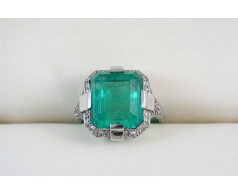 AN EMERALD AND DIAMOND CLUSTER RING the cut cornered rectangular-shaped emerald weighs 9.02 carats and is set within a surrou