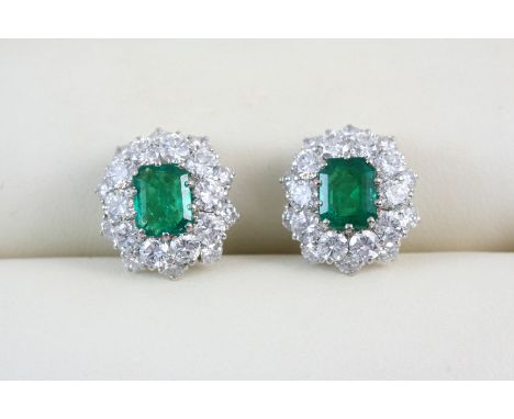 A PAIR OF EMERALD AND DIAMOND CLUSTER EARRINGS each set with a cut-cornered rectangular-shaped emerald within a surround of c