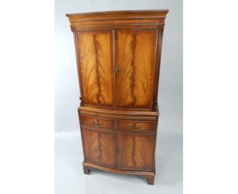 A mahogany serpentine cocktail cabinet, with a pair of doors enclosing shelves, over a brushing slide, pair of frieze drawers