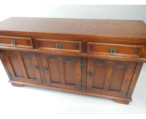 An Old Charm oak sideboard, with three frieze drawers over cupboards with Gothic arch tracery doors, raised on bracket feet, 