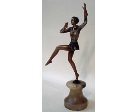 An Art Deco bronze patinated spelter figural model of a female dancer in a jacket and short skirt, set on a circular onyx col