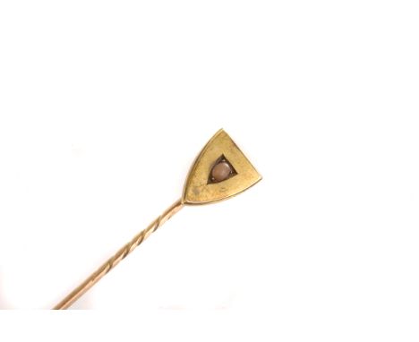 A gold and coral tie pin, the shield shaped terminal having central oval cut coral stone