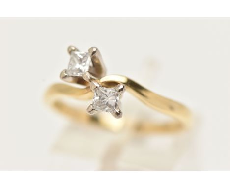 AN 18CT GOLD DIAMOND CROSS OVER RING, designed as two princess cut diamonds each in a four claw setting, together with two In