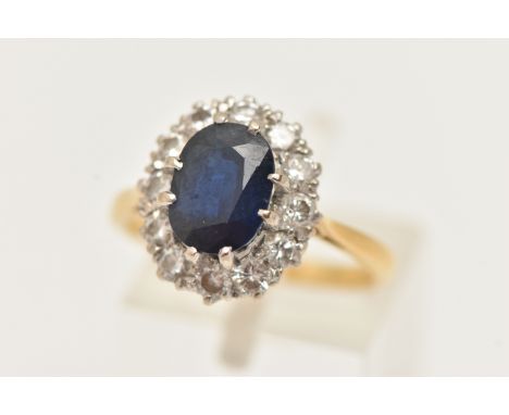 A YELLOW METAL SAPPHIRE AND DIAMOND CLUSTER RING, set with a central oval cut deep blue sapphire, double four claw setting, w