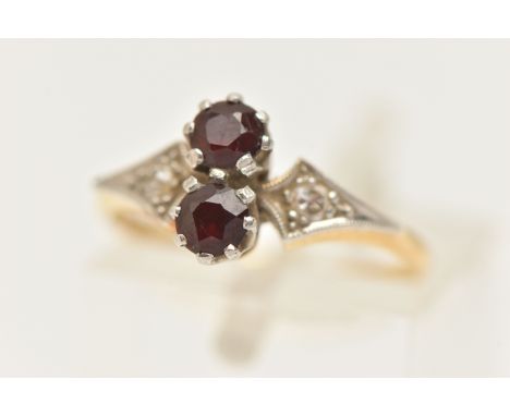 A YELLOW METAL AND GARNET RING, set with two circular cut garnets each in an eight claw white metal setting, flanked with rou