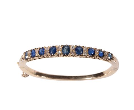 A SAPPHIRE AND DIAMOND HINGED BANGLE half set with nine graduated sapphires divided with round-cut diamonds, on unmarked yell