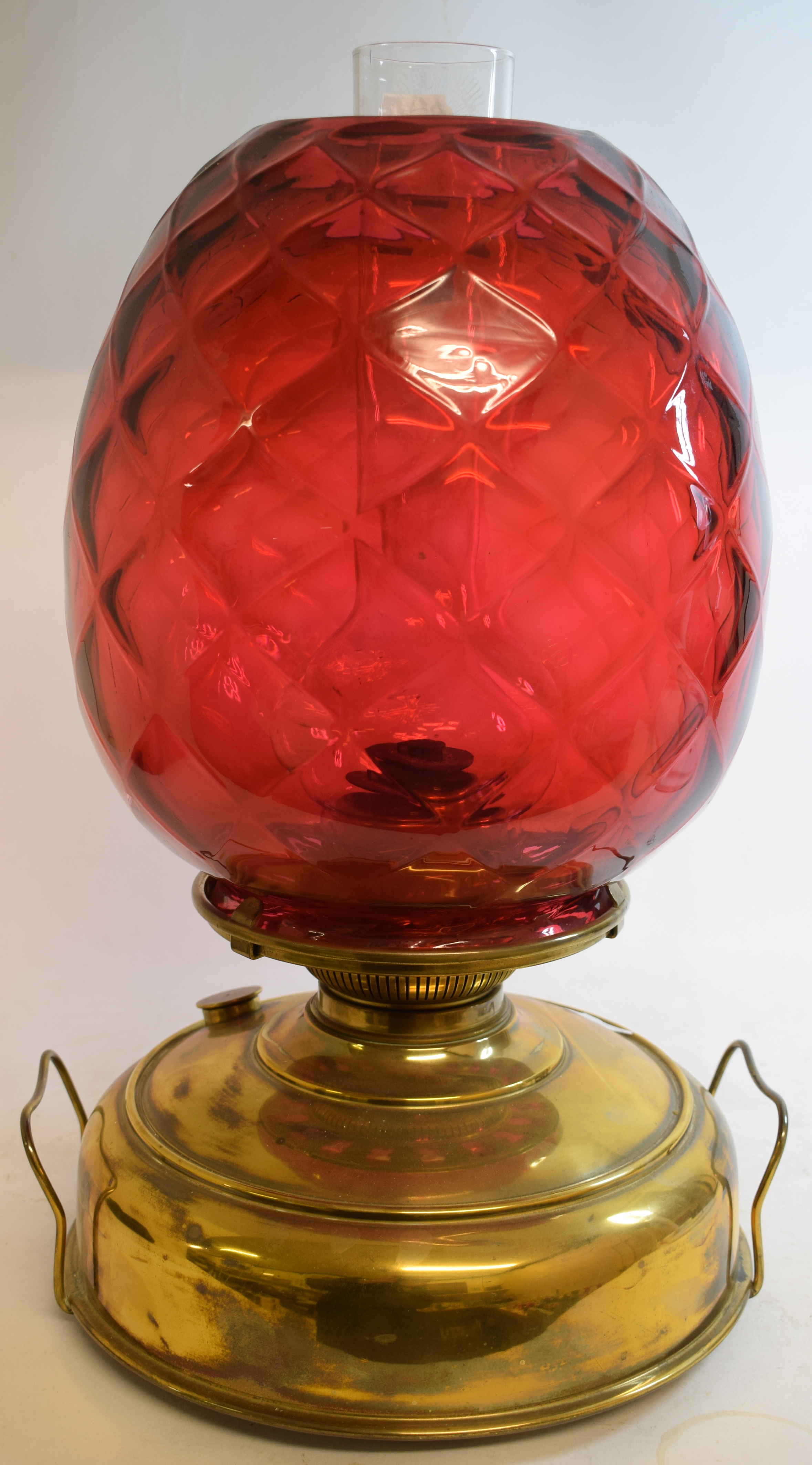 A large oil lamp, with a quilted cranberry glass shade on a brass