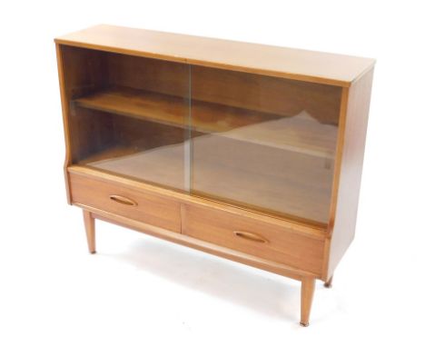 A mid century teak display cabinet, with two sliding glazed doors and single shelf, above a pair of frieze drawers, raised on