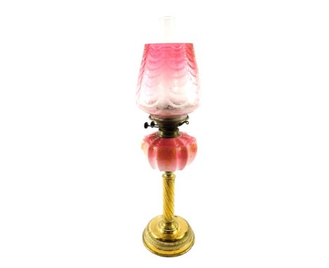 A Victorian brass oil lamp, with an enamel decorated Burmese glass reservoir, glass chimney and floral etched clear to cranbe