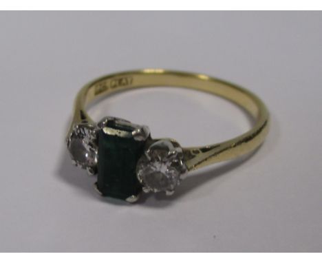 A three stone emerald and diamond ring, the rectangular step cut emerald flanked to either side by a round brilliant cut diam