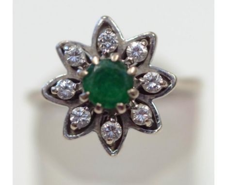 A diamond and emerald flower head cluster ring, the white mount stamped '18ct', the round cut emerald enclosed by eight brill