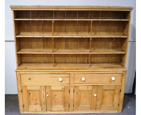 A late Victorian pine dresser with raised plate rack above two deep drawers above four panelled doors with white ceramic hand