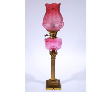 A Victorian brass oil lamp, with engraved cranberry glass shade and reservoir, upon a Corinthian column and stepped square ba