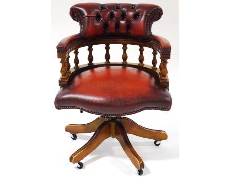 A leather and mahogany Captain's chair with button back on splayed legs with casters