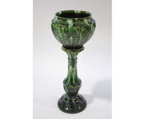 A Victorian pottery jardinere on stand with bottle green glaze, panels of plant decoration in relief and Classical ornamentat