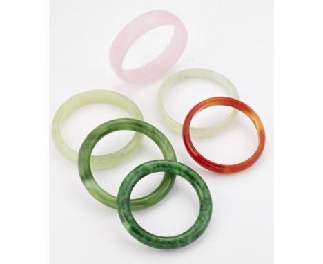 A GROUP OF FIVE JADE AND OTHER HARDSTONE BANGLES AND A GREEN GLASS BANGLE.&nbsp;Measure 6.5cm in diameter and smaller (6)