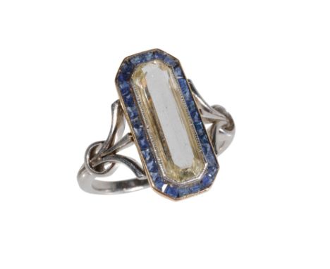 DIAMOND AND SAPPHIRE RING, the large elongated emerald-cut diamond, within a border of princess-cut sapphires, on an unmarked