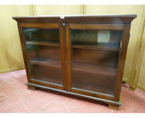 A LOW TWO DOOR BOOKCASE with twin glass doors and fixed interior shelves on bracket corner feet, 84 cms high, 107 cms wide, 2