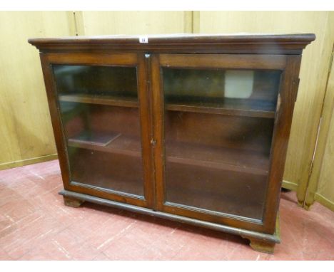 A LOW TWO DOOR BOOKCASE with twin glass doors and fixed interior shelves on bracket corner feet, 84 cms high, 107 cms wide, 2