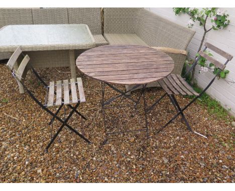 A vintage garden table with two chairs, with metal frames and wooden slats, table diameter approximately 80 cm, in a weathere