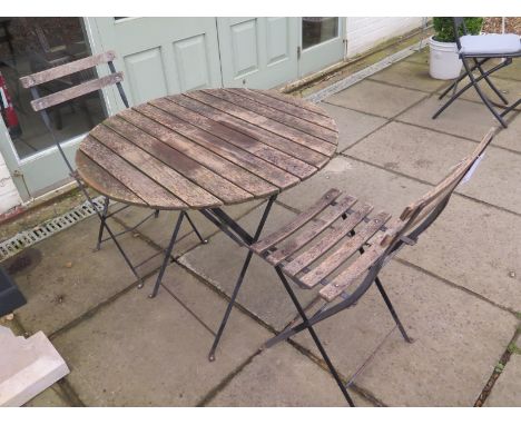 A vintage garden table with two chairs, with metal frames and wooden slats, table diameter approximately 80 cm, in a weathere