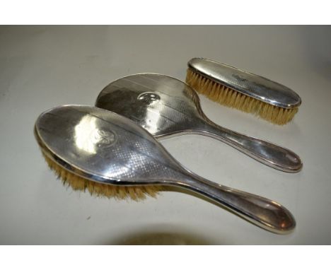 An engine turned silver three piece dressing table set, by D M Co, Birmingham 1934, comprising hand mirror and two brushes. C