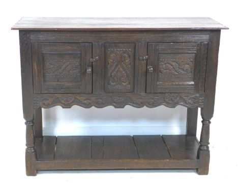 A Jacobean style oak small sideboard, with carved decoration and chip carved ends, swivel toggles to doors, raised on turned 