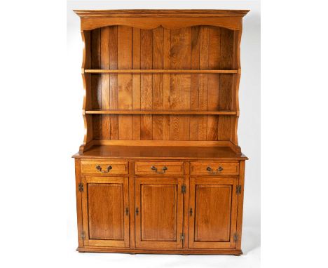 A reproduction oak dresser with shaped canopy and enclosed back with two shelves over a rectangular top and three moulded dra