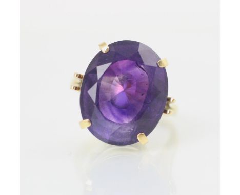 An untested amethyst set cocktail ring, the oval cut stone within yellow metal claw setting leading to plain polished shank, 